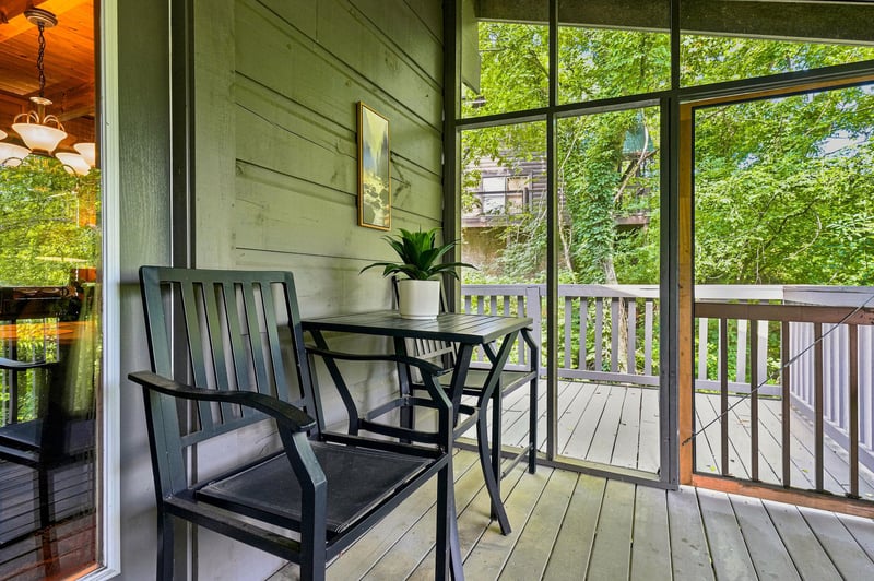 Enjoy your morning coffee on this peaceful screened porch surrounded by lush greenery, where a cozy chair and table create the perfect retreat for unwinding in nature.