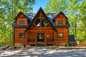 Beautiful log cabin retreat nestled among towering trees, featuring classic mountain architecture with a welcoming covered porch.