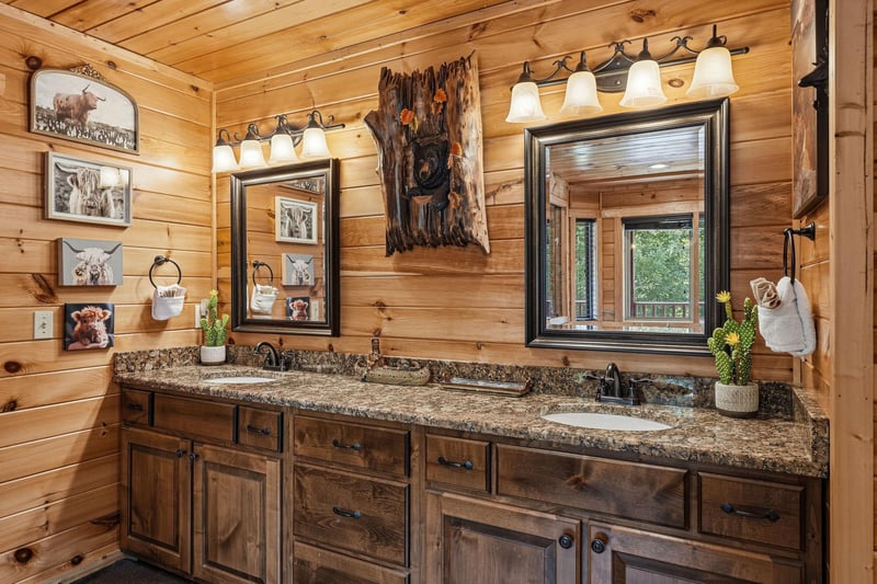 Your rustic bathroom features double vanities with granite countertops, framed mirrors, and charming woodlandthemed décor—a cozy retreat after your adventures.