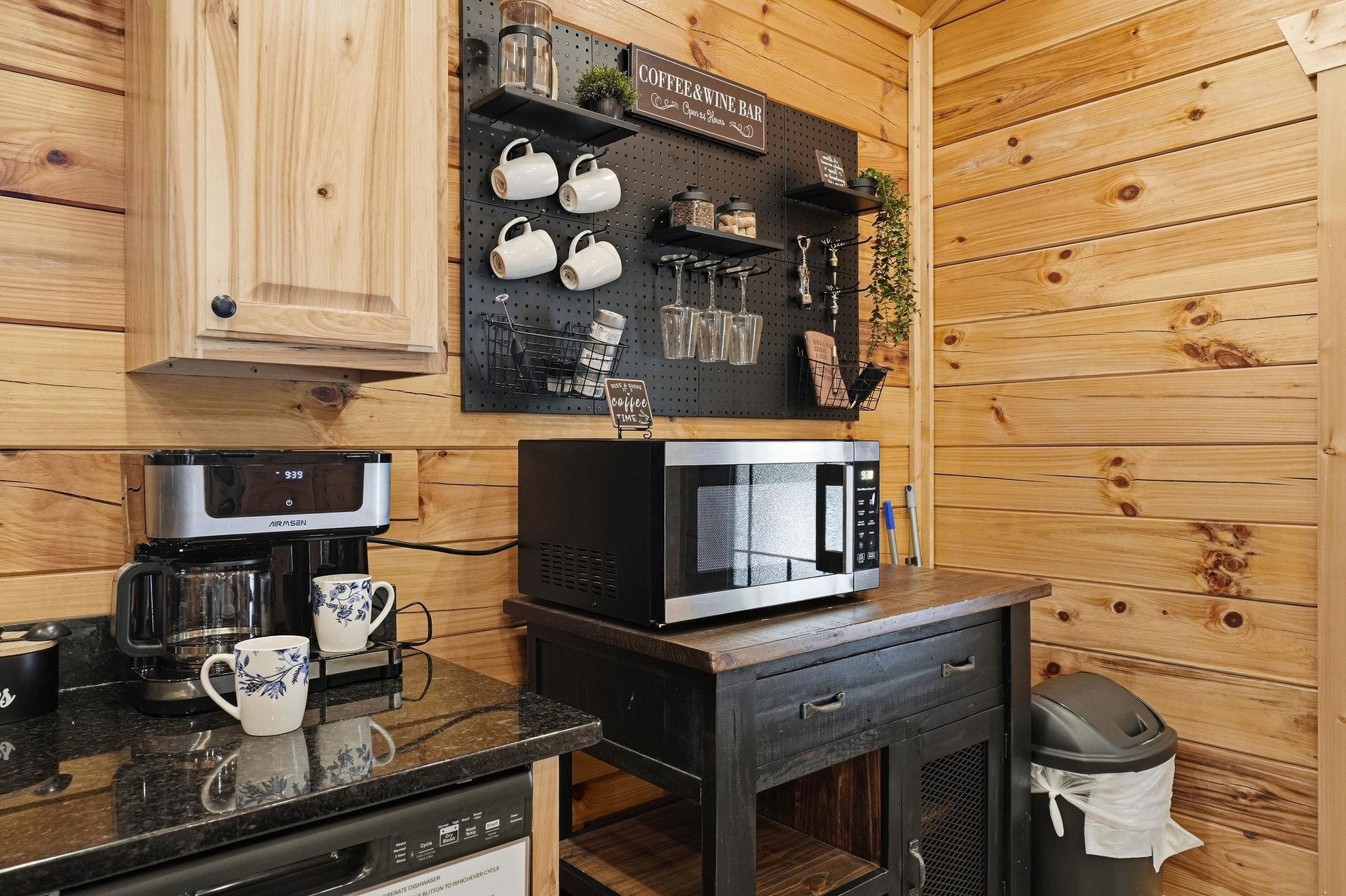 Your cozy cabin kitchen features warm wood walls, a dedicated coffee bar with hanging mugs, and modern appliances ready for your morning brew or quick meal prep.