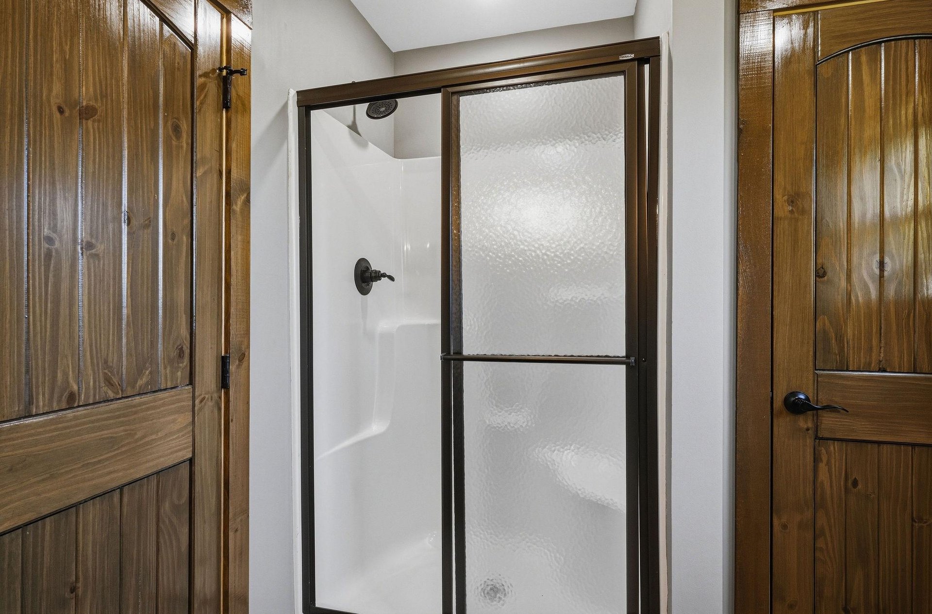 Step into your own private shower with sliding glass doors and warm rustic accents. The natural wood cabinetry adds a cozy cabin charm to your bathroom retreat.