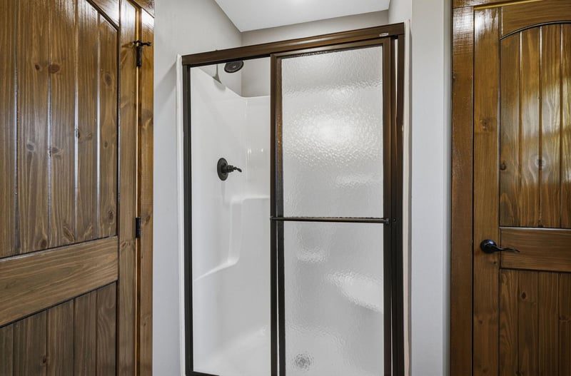 Step into your own private shower with sliding glass doors and warm rustic accents. The natural wood cabinetry adds a cozy cabin charm to your bathroom retreat.