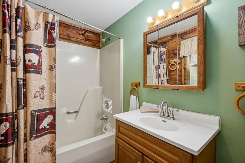 Refresh in this charming bathroom featuring rustic wood vanity, soothing green walls, and wildernessthemed shower curtain that creates a cozy cabin feel.