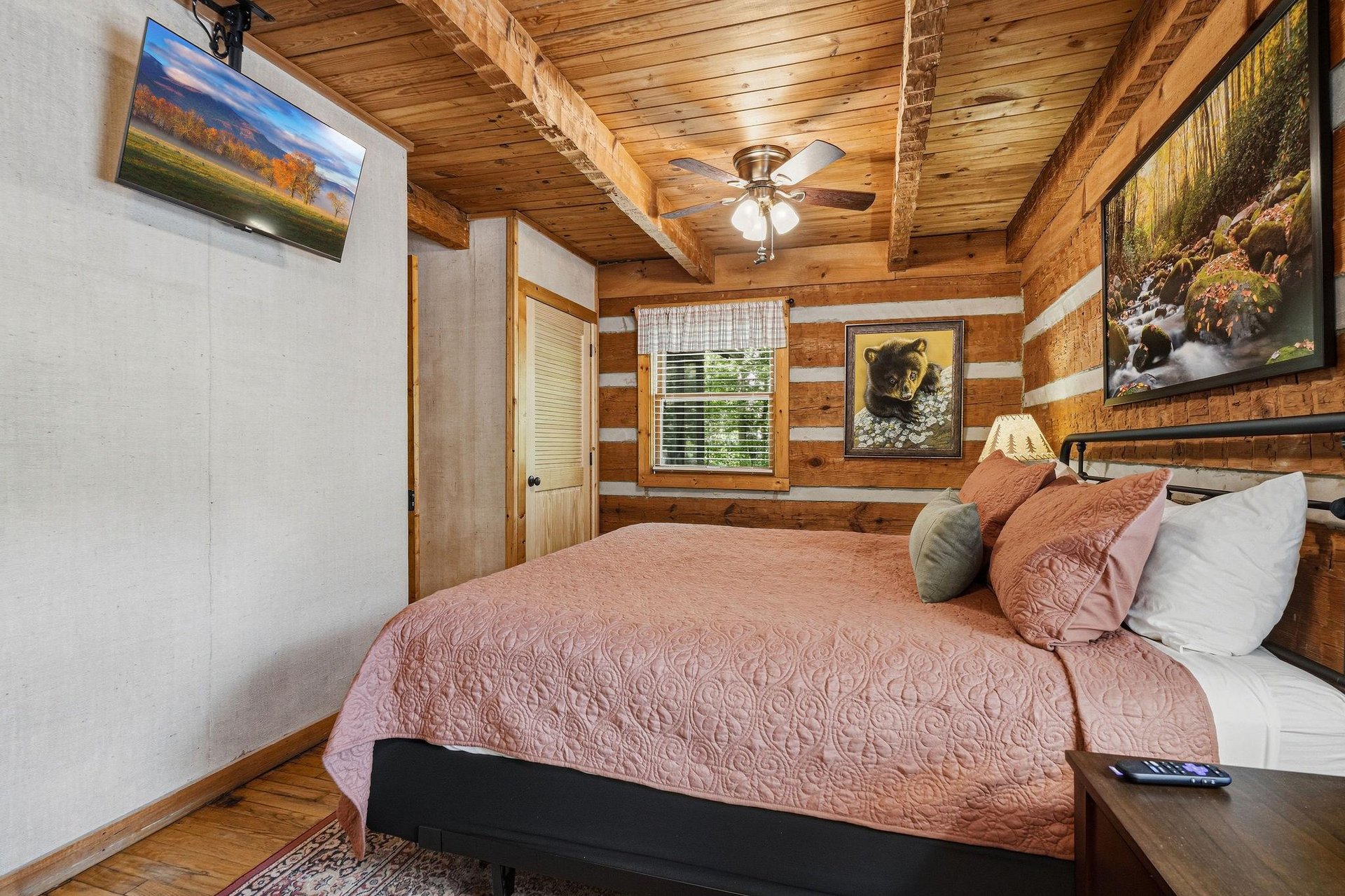 Unwind in this rustic bedroom where wood beams frame your peaceful retreat. Sink into soft bedding as natural light filters through the window, illuminating wildlife art that brings the outdoors in.