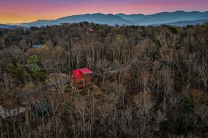 Stunning mountain cabin nestled among autumn trees with breathtaking sunset views over rolling peaks.