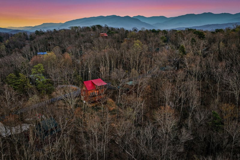 Stunning mountain cabin nestled among autumn trees with breathtaking sunset views over rolling peaks.