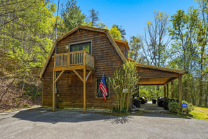 Charming wooden cabin surrounded by lush forest, featuring a private balcony and covered parking area.