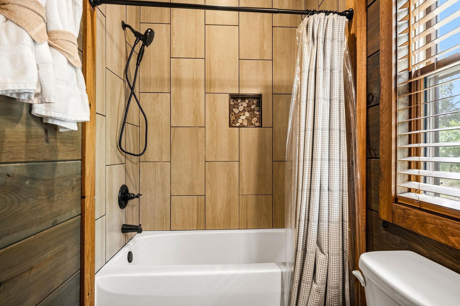Step into your rusticmodern bathroom with natural wood accents, a sleek tiled showertub combo, and a cozy window view perfect for unwinding.