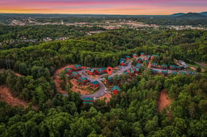 Stunning aerial view of the cabin resort community nestled in lush forests, with mountain vistas and vibrant sunset skies painting the horizon over the charming neighborhood.