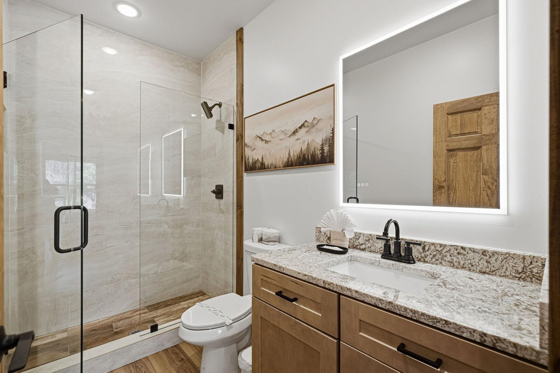 Unwind in your spalike bathroom featuring granite counters, modern shower, and mountain artwork that brings nature indoors.