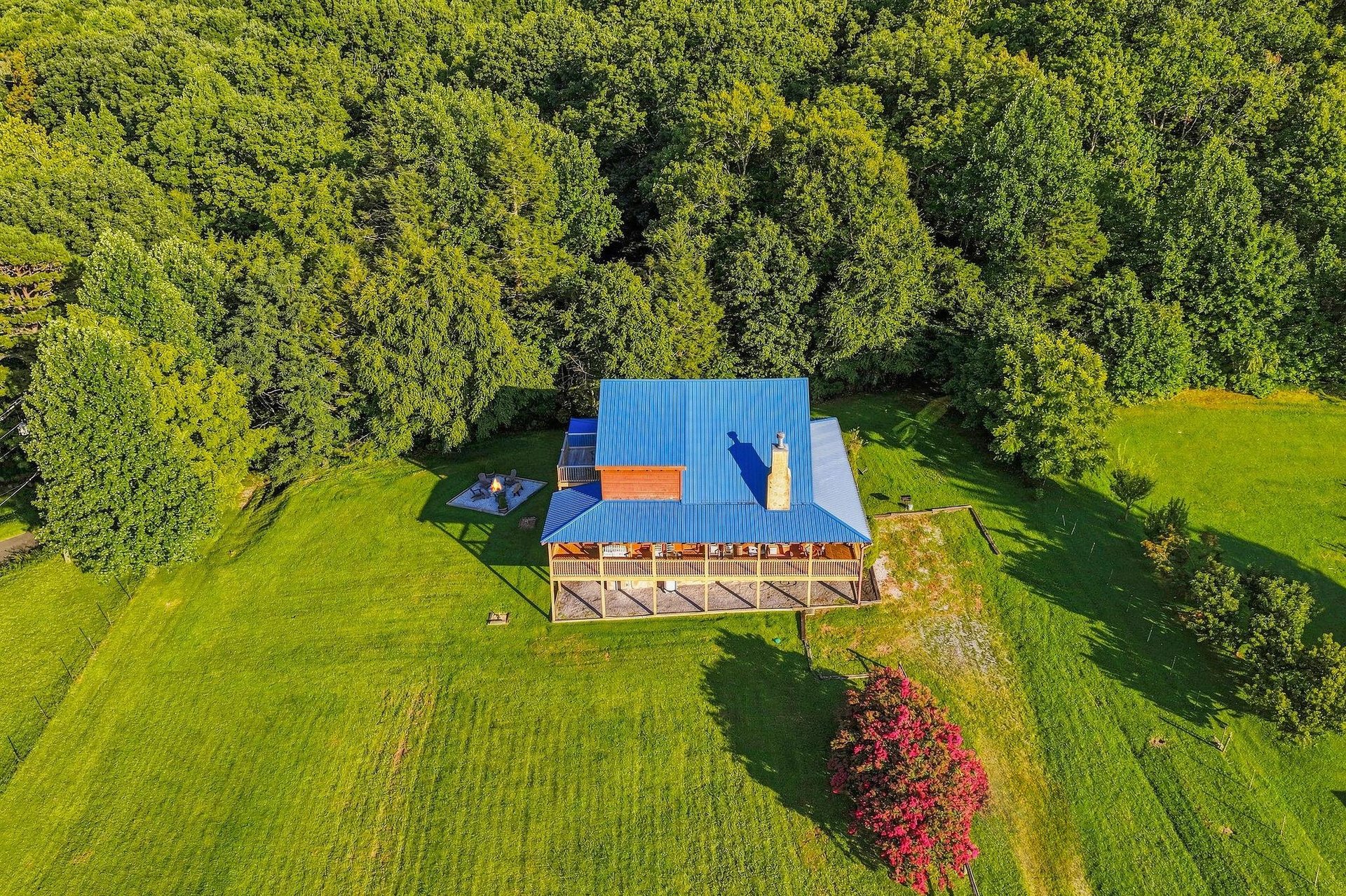A charming property nestled on spacious grounds, surrounded by lush forest and vibrant seasonal foliage. The blue roof and wraparound deck stand out beautifully against the natural landscape.
