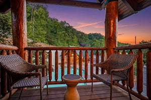 Sunset view from a private balcony overlooking the pool and natural landscape, framed by rustic log columns with comfortable wicker seating inviting peaceful mountain evenings.