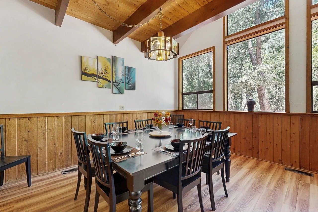 The dining table seats the whole group in style, with tall windows framing the surrounding pines — a great spot for family dinners after a day in Idyllwild.