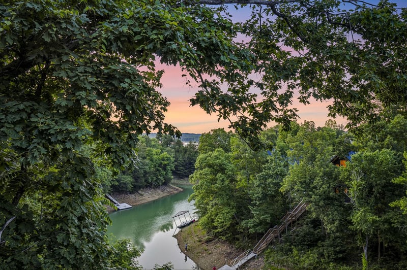 Scenic lake cove framed by lush trees at sunset, with private docks along the peaceful shoreline and rolling hills in the distance.