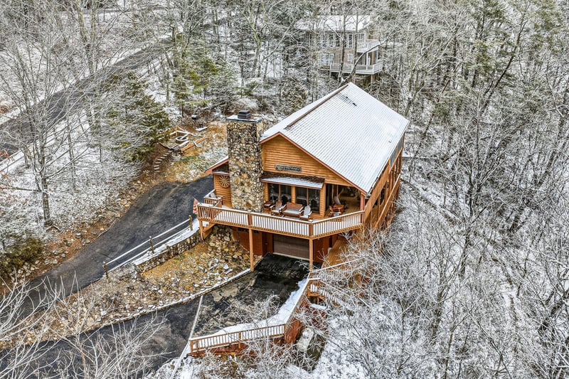 Rustic cabin nestled in snowdusted forest with wraparound deck and natural stone chimney creates a perfect winter retreat.