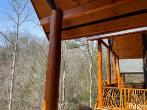Rustic wooden covered deck overlooks peaceful wooded valley with bare winter trees and blue sky.
