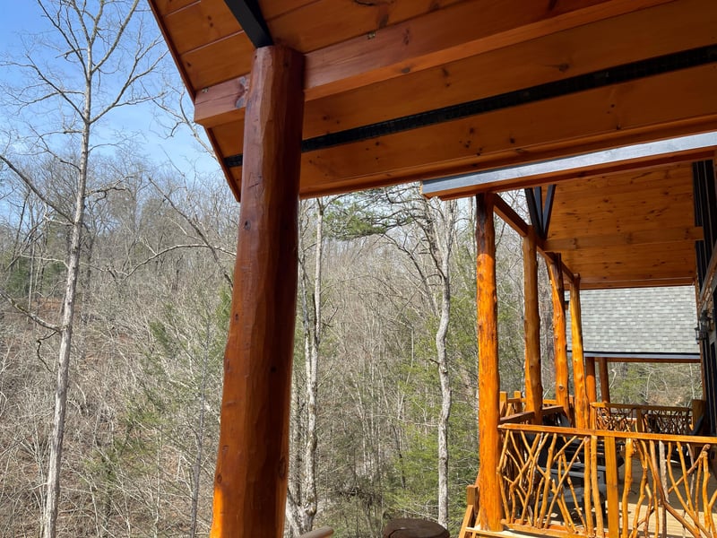 Rustic wooden covered deck overlooks peaceful wooded valley with bare winter trees and blue sky.