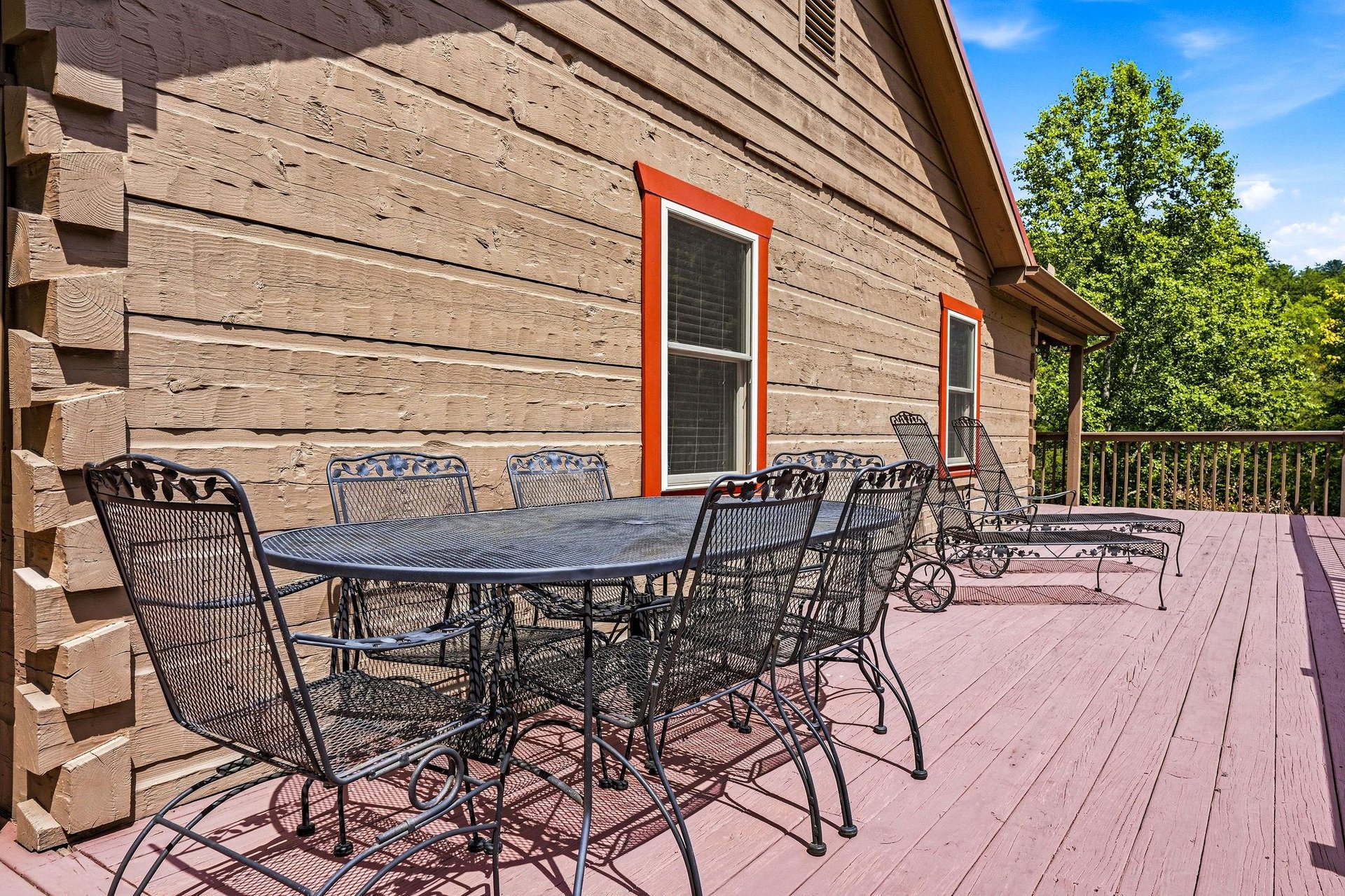 A spacious deck with dining and lounging areas, framed by natural wood siding and surrounded by lush greenery, invites you to relax outdoors in comfort.
