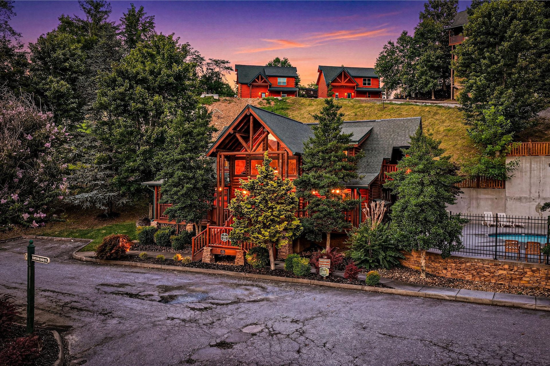 Stunning sunset illuminates the propertys exterior, nestled among lush trees in a peaceful neighborhood setting, marking the welcoming start to your mountain getaway.