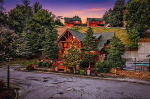 Stunning sunset illuminates the propertys exterior, nestled among lush trees in a peaceful neighborhood setting, marking the welcoming start to your mountain getaway.