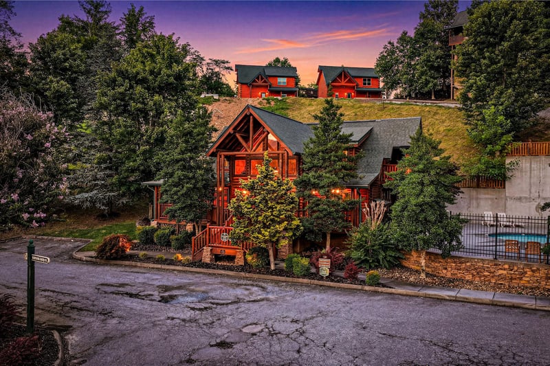 Stunning sunset illuminates the propertys exterior, nestled among lush trees in a peaceful neighborhood setting, marking the welcoming start to your mountain getaway.