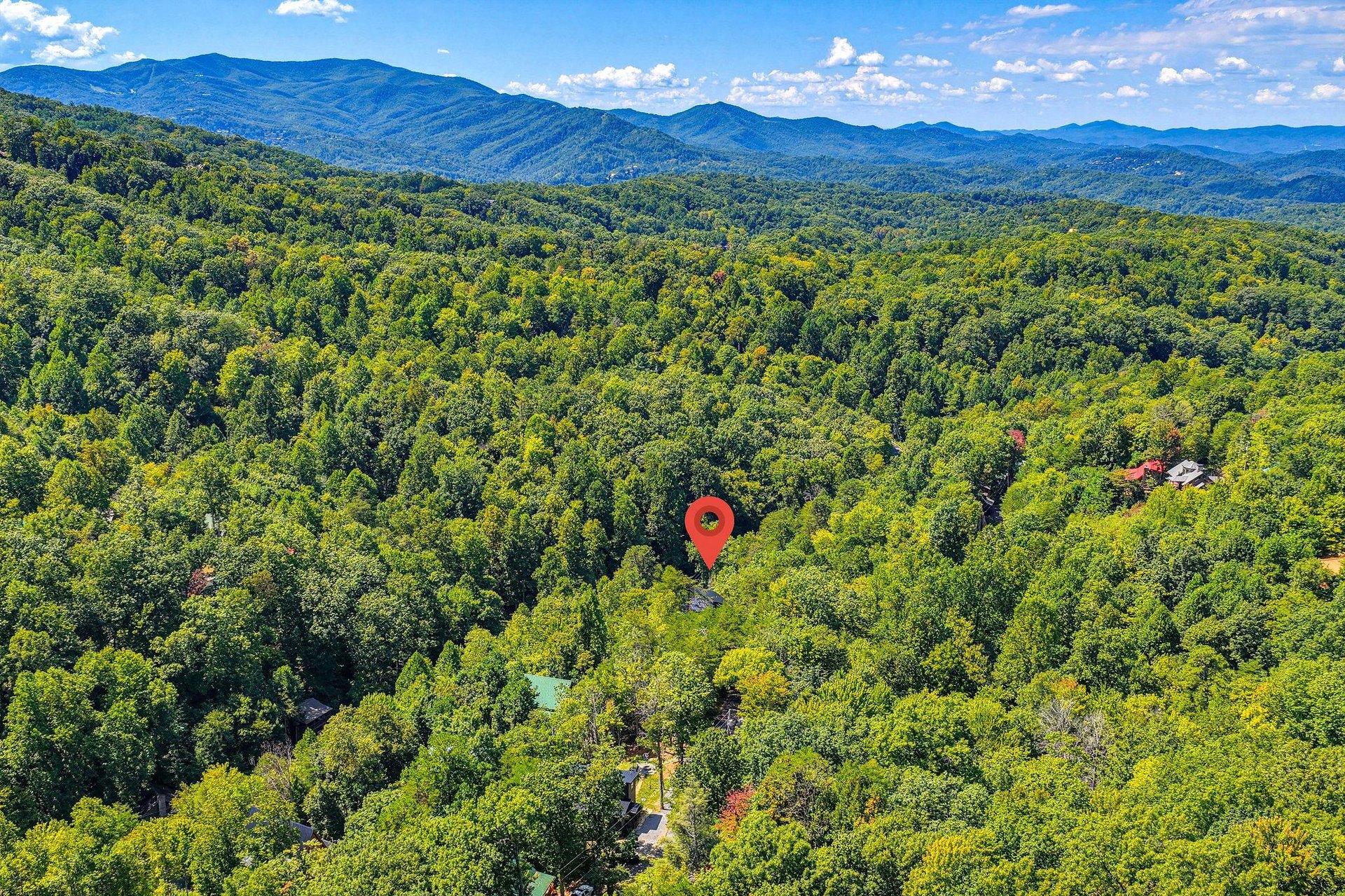 Aerial view showcasing the property nestled among dense forest, with the Blue Ridge Mountains rising majestically in the background under a bright, clouddappled sky.