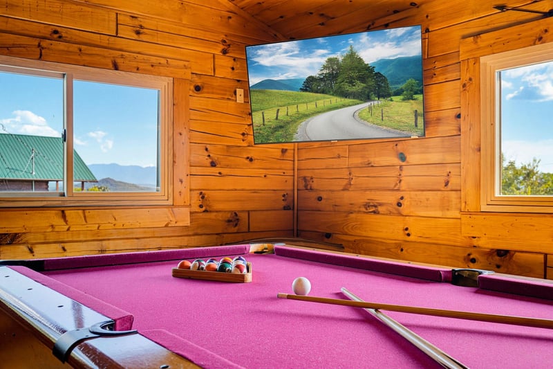 Challenge your travel companions to a game on the pinkfelted billiard table in this cozy cabin game room, surrounded by warm wood and mountain views.