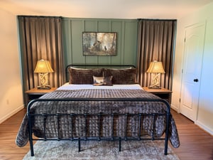 Sink into your plush quilted bed framed by soft lighting and serene sage tones, where rustic charm meets restful elegance in your private retreat.