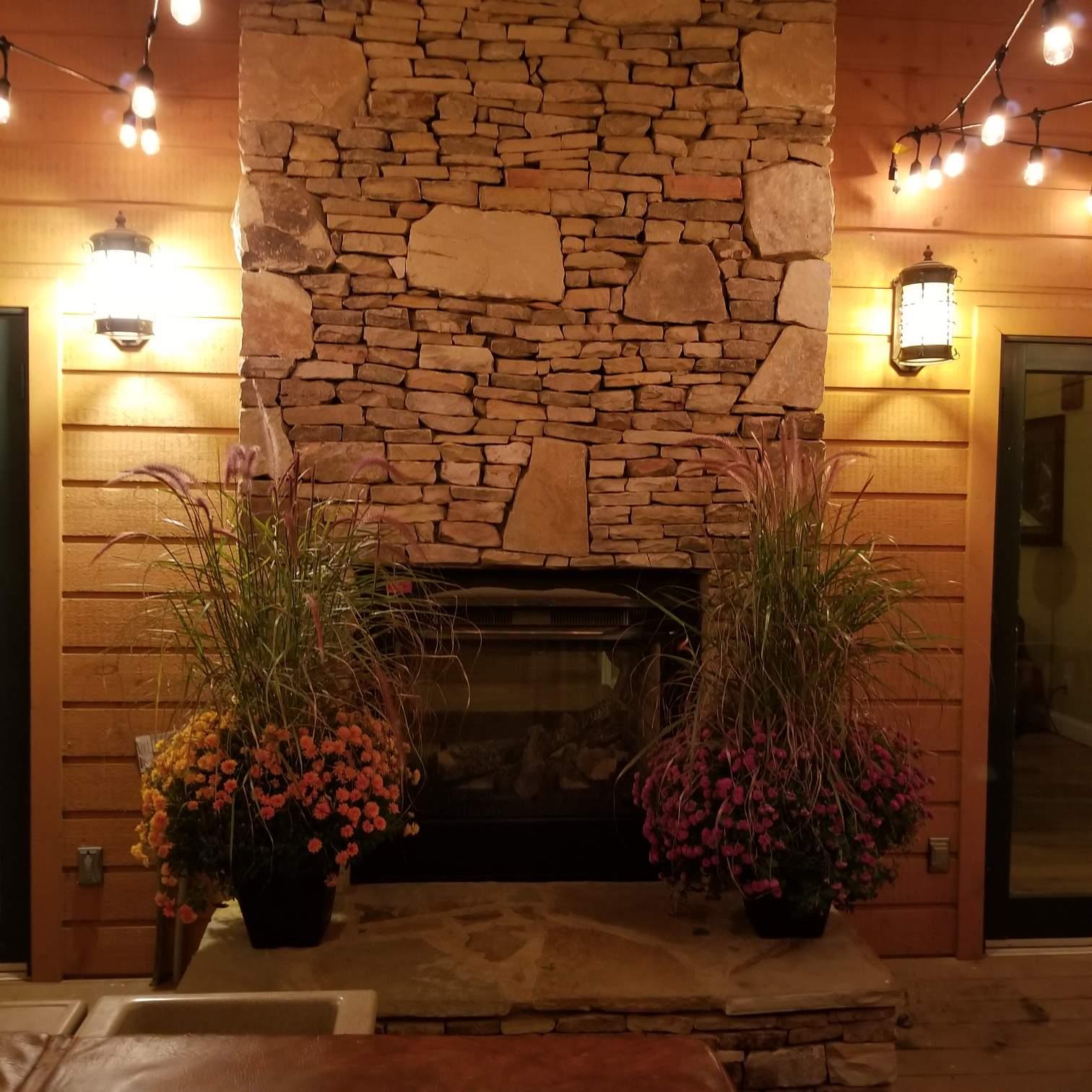 A rustic stone fireplace anchors this inviting space, flanked by seasonal blooms and warm wood paneling that creates a cozy mountain retreat ambiance.