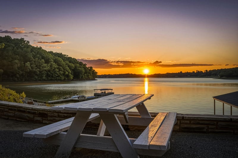 A tranquil lakeside setting at golden hour, with a private dock and peaceful waters framed by lush forested shores and vibrant sunset skies.