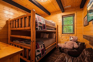 Cozy log cabin bedroom with rustic bunk beds and a friendly teddy bear awaiting your familys arrival.