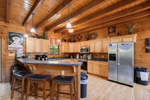 Gather around the kitchen island where rustic charm meets modern comfort, inviting you to share morning coffee and stories under soaring woodbeamed ceilings.