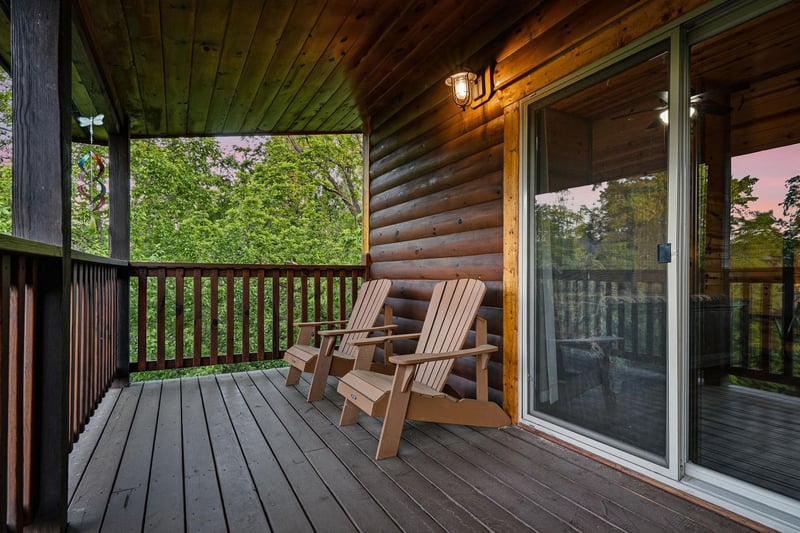 Unwind on your private deck with Adirondack chairs overlooking lush greenery, where warm cabin lighting creates the perfect evening retreat.