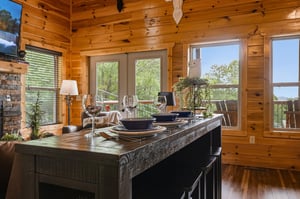 Picture yourself savoring breakfast at this rustic wooden table, sunlight streaming through expansive windows framing lush forest views. The cozy cabin atmosphere invites relaxation and memorable meal