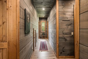 A warm hallway with rustic woodpaneled walls and ceiling leads to a peaceful nook, complete with a cozy reading chair and colorful runner beneath your feet.