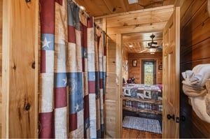 Step into this cozy cabin bedroom where rustic charm meets comfort. Natural wood walls surround you, while a ceiling fan keeps things cool. The plaid bedding invites restful nights under the stars.