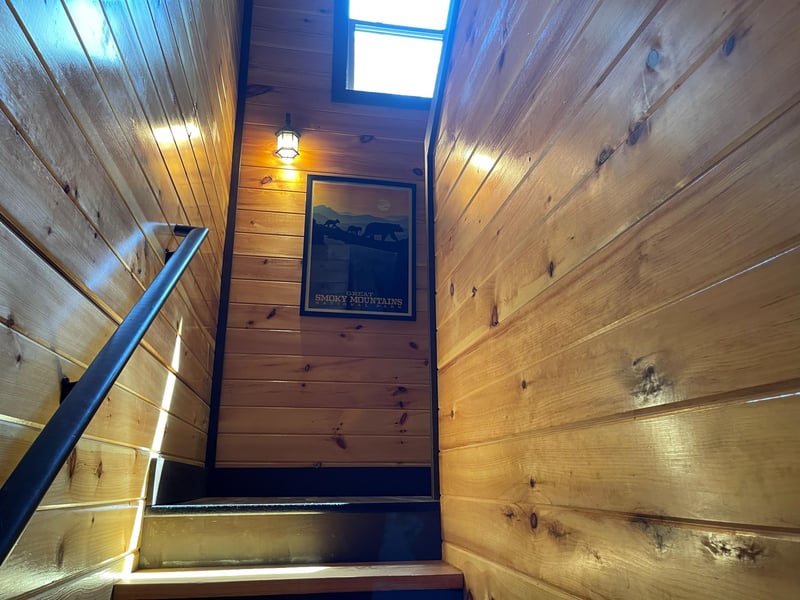 Climb the rustic wood stairway bathed in natural light from the skylight above, where warm paneling and thoughtful decor welcome you to your mountain retreat.