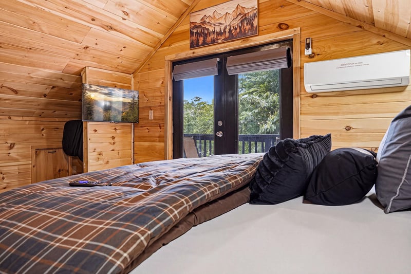 Wake up to natural light streaming through your private balcony doors, with treetop views welcoming your morning. The warm woodpaneled walls and vaulted ceiling create a cozy mountain retreat feel, w