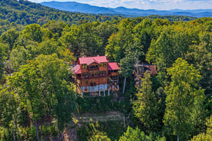 A striking log cabin with a vibrant red roof nestled in a wooded mountain setting, offering seclusion and natural beauty in the surrounding landscape.
