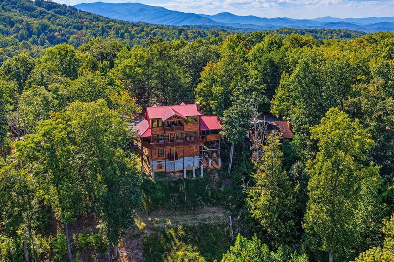 A striking log cabin with a vibrant red roof nestled in a wooded mountain setting, offering seclusion and natural beauty in the surrounding landscape.