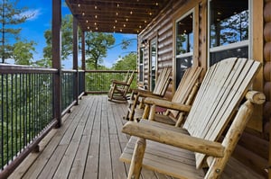 Unwind on the covered deck with rustic rocking chairs, string lights overhead, and peaceful views of the surrounding trees—your perfect spot to relax and breathe in the fresh mountain air.
