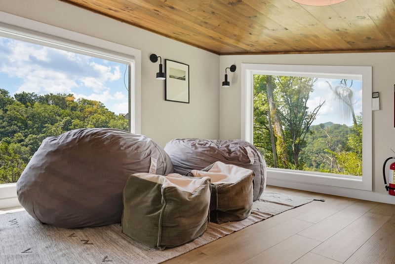 Sink into plush bean bags beneath the warm rustic wood ceiling as expansive windows frame lush forest views and natural light fills your cozy retreat.
