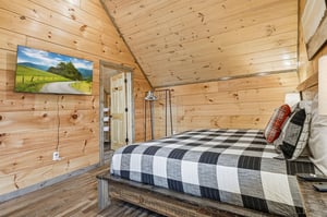 Cozy rustic bedroom with warm wood walls, flatscreen TV, and comfortable plaid bedding for your mountain retreat.