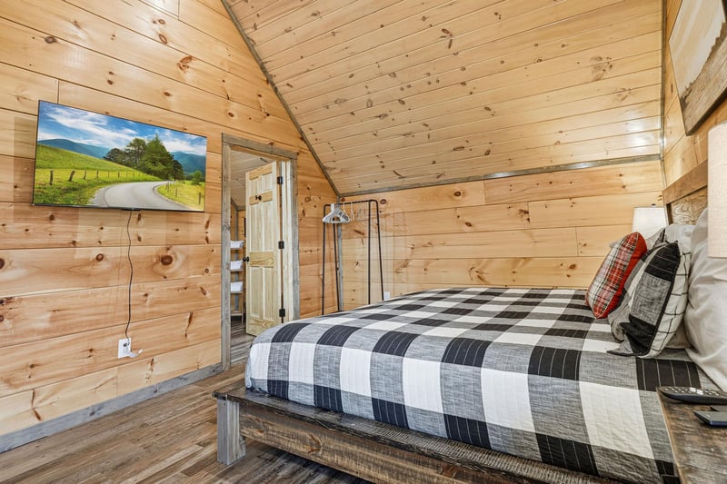 Cozy rustic bedroom with warm wood walls, flatscreen TV, and comfortable plaid bedding for your mountain retreat.