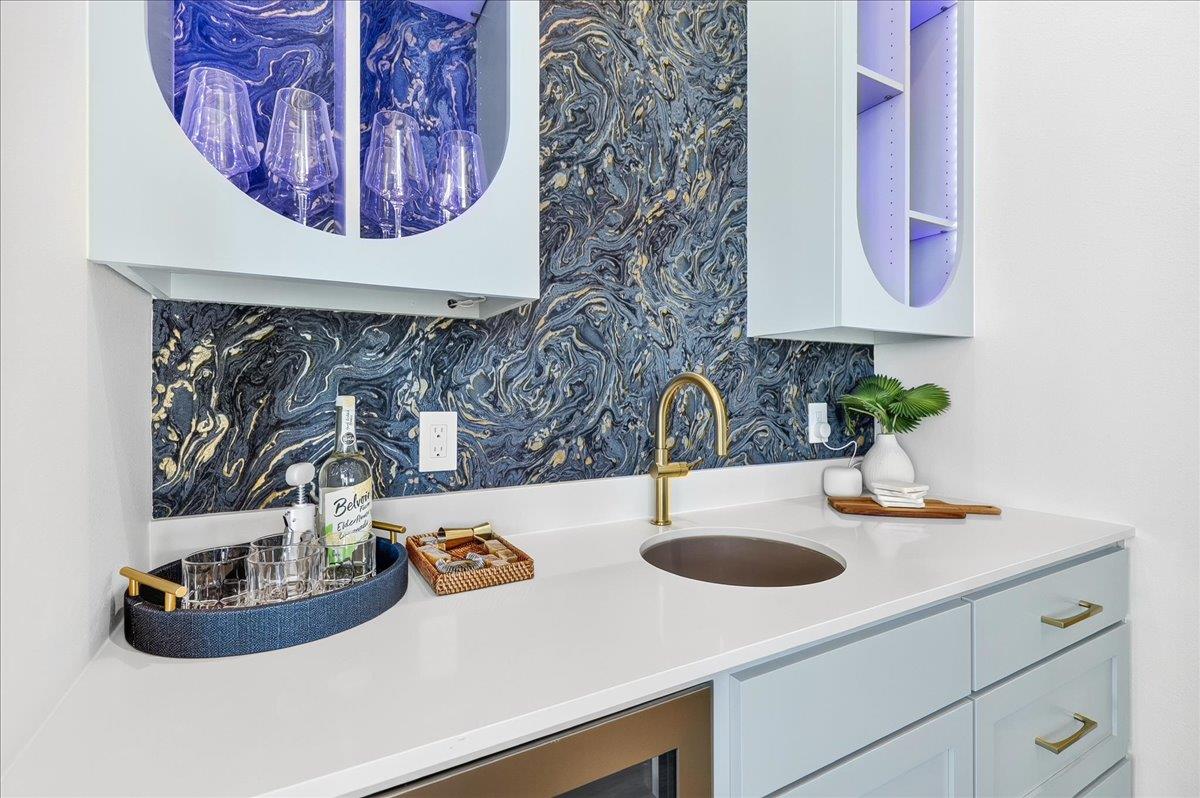 Featuring custom cabinetry, elegant countertops, and ambient lighting, this stylish wet bar offers open shelving for glassware and spirits, plus a builtin beverage refrigerator for effortless enterta