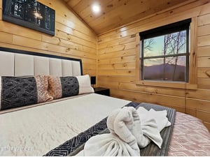 Sink into this cozy cabin bedroom where warm wood walls embrace you and mountain views greet your mornings through the bedside window.