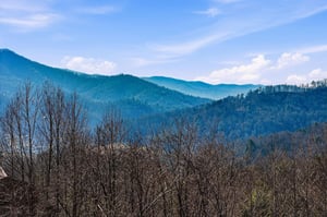 Rolling mountain ridges stretch across the horizon, creating layers of bluetinted peaks beneath a cloudy sky.