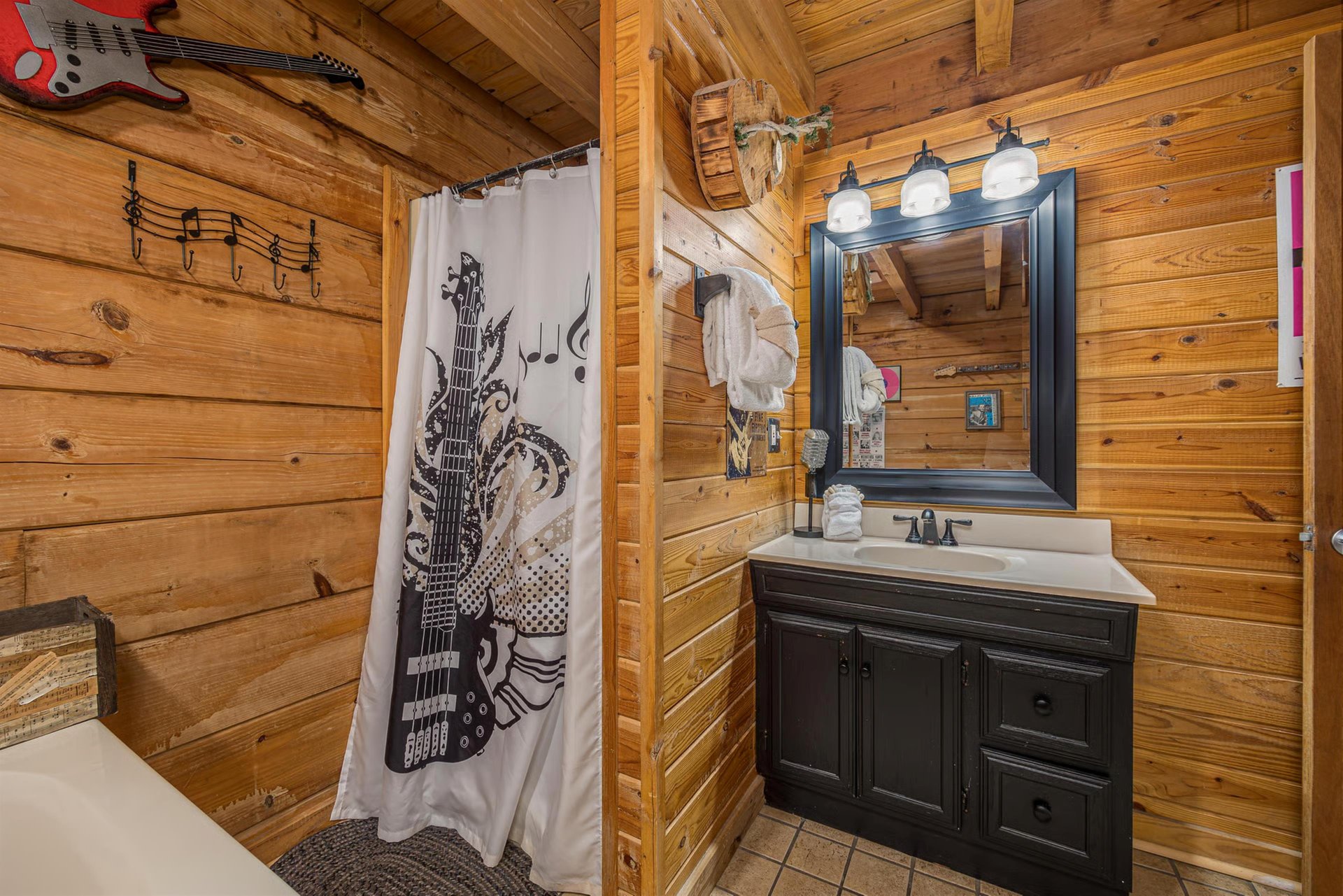 Rock out in your private bathroom featuring rustic wood walls, artistic guitarthemed shower curtain, and charming cabinstyle vanity.