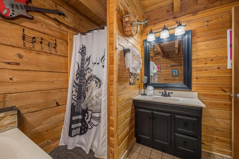 Rock out in your private bathroom featuring rustic wood walls, artistic guitarthemed shower curtain, and charming cabinstyle vanity.