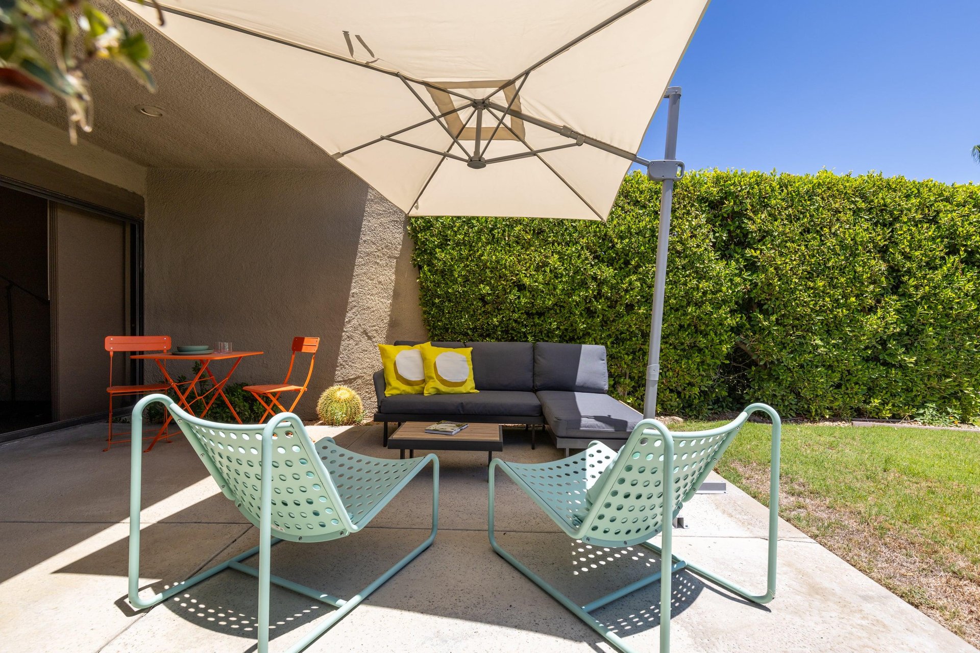Back patio located off of the living room and primary bedroom featuring a table and chairs for morning coffee, umbrella, and ample outdoor seating.